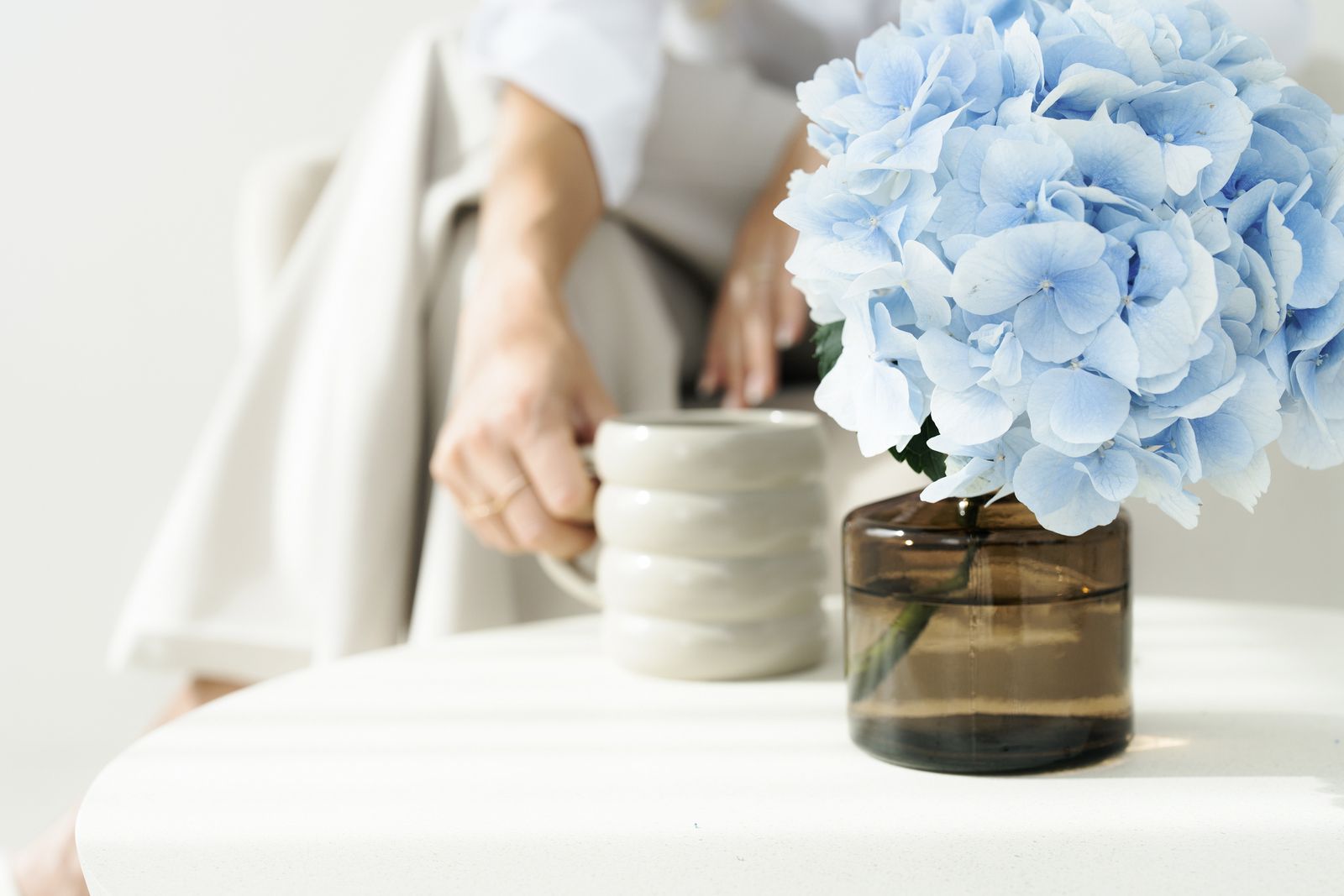 Hände mit einer Tasse, davor eine blaue Hortensie